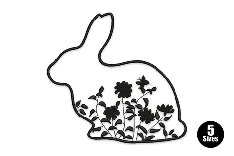 Rabbit outline embroidery with wildflowers, stems and a small butterfly growing inside the bunny silhouette, single black thread on white fabric.